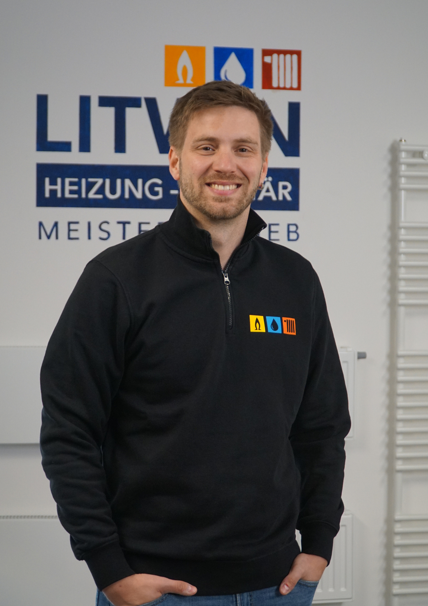 Fabian Kronbach (operat. Leitung) vor dem Logo von Litwin Heizung Sanitär. Im Hintergrund sind verschiedene Heizkörper.