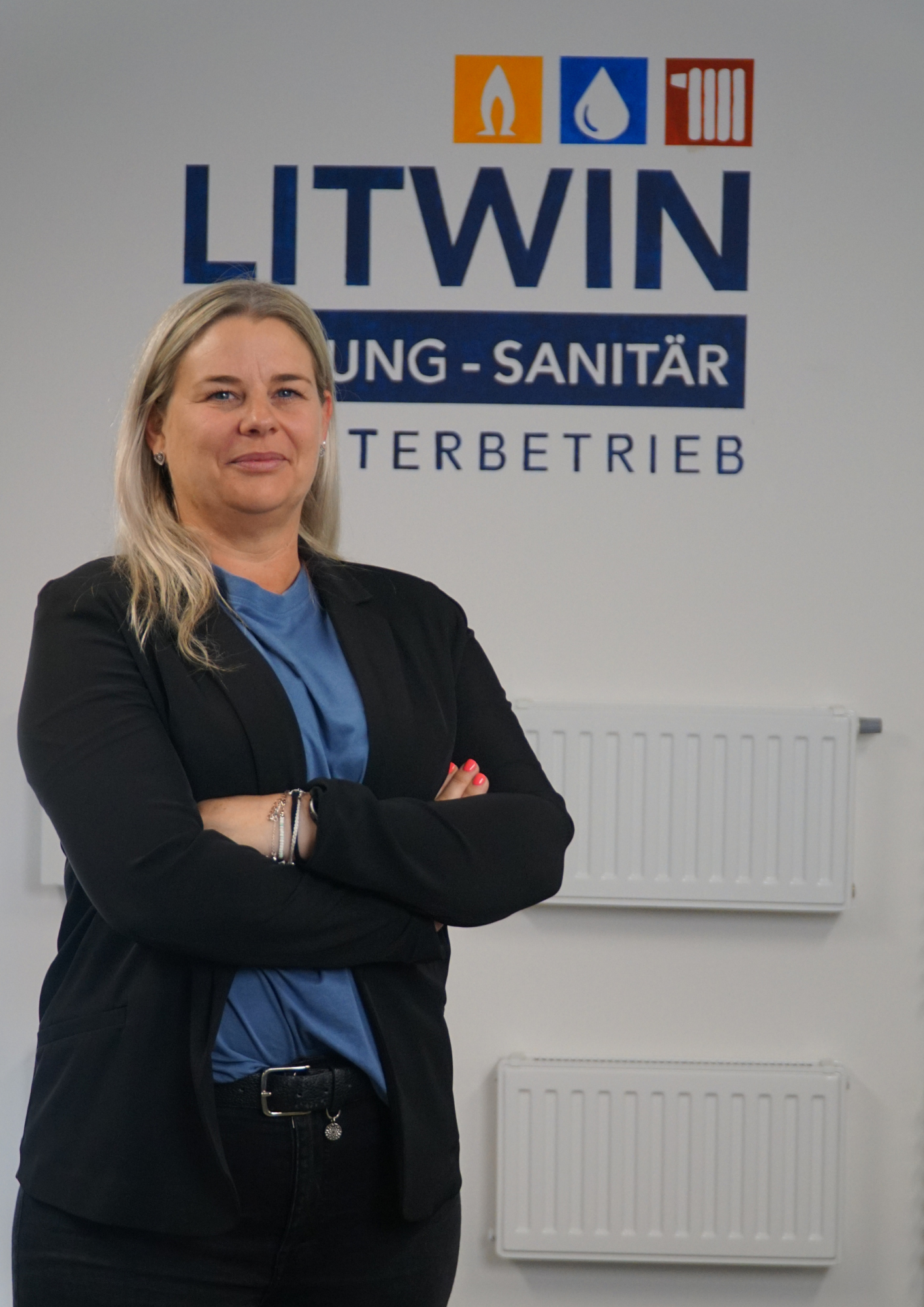 Sabrina Litwin (Prokuristin) vor dem Logo von Litwin Heizung Sanitär. Im Hintergrund sind verschiedene Heizkörper.